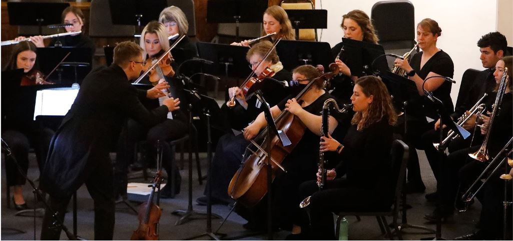 A symphonic orchestra dressed all in black playing a concert.