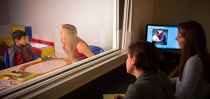 Student working with young child in the Center for Speech, Language and Hearing Disorders while other students observe