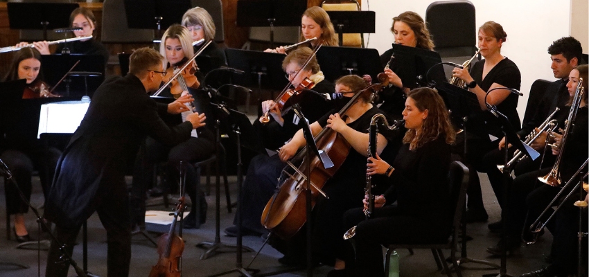 A symphonic orchestra dressed all in black playing a concert.