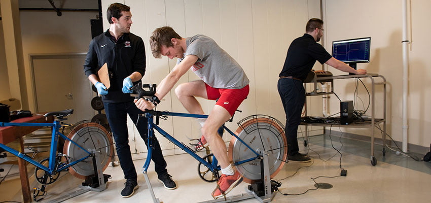 Kinesiology graduate students working with graduate student on a bicycle in the Exercise Physiology Lab in the Professional Studies building.