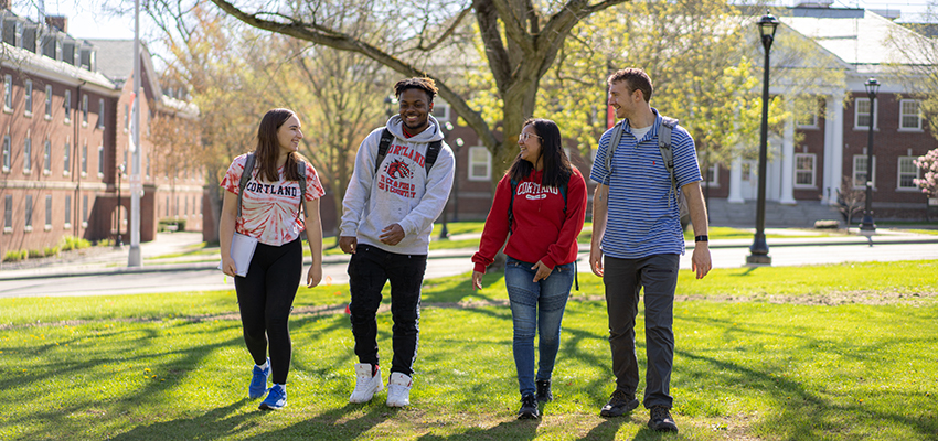 Group of four students walking together on Moffett lawn with Brockway Hall in the background