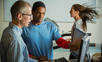 Kinesiology professor and student looking at a monitor while another student runs on a treadmill