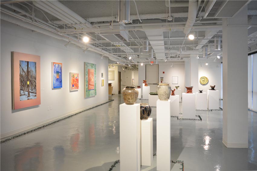 View into the central gallery at Dowd Gallery featuring sculptural objects produced by Jeremiah Donovan, professor of ceramics, Jillian McEvoy, instructor of ceramics, paintings by Stephen Alexander Clark, processor of painting, and floor installation by Bryan Valentine Thomas, instructor of design and drawing, at the Art and Art History Department.  